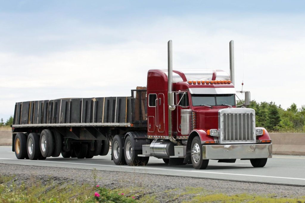 Red semi truck with flatbed trailer on a highway.