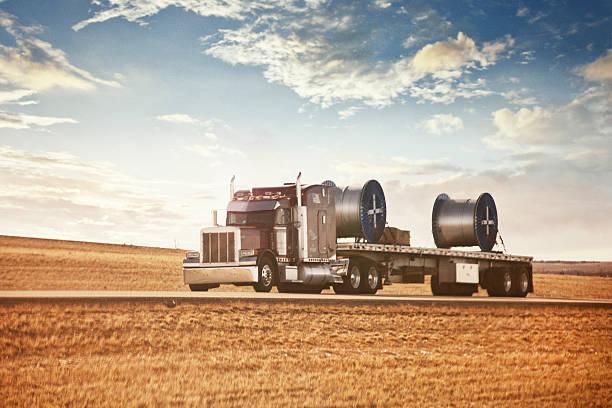 Semi truck hauling large industrial spools on a flatbed trailer.